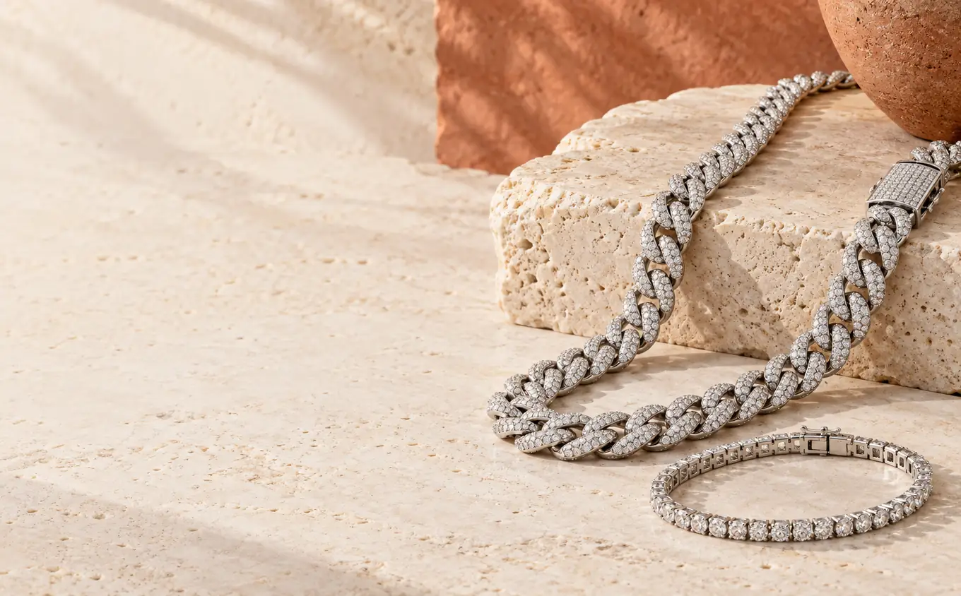 Iced-out Cuban chain and tennis bracelet concept on warm ivory stone.